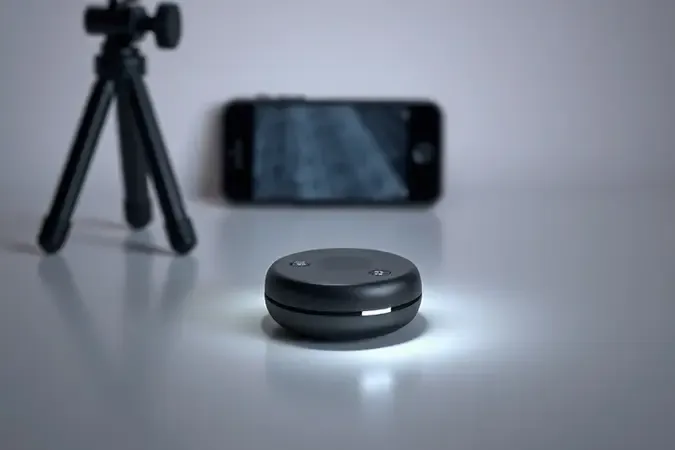Controle remoto bluetooth em primeiro plano ao lado de tripé para celular desfocado ao fundo em composição 3D minimalista